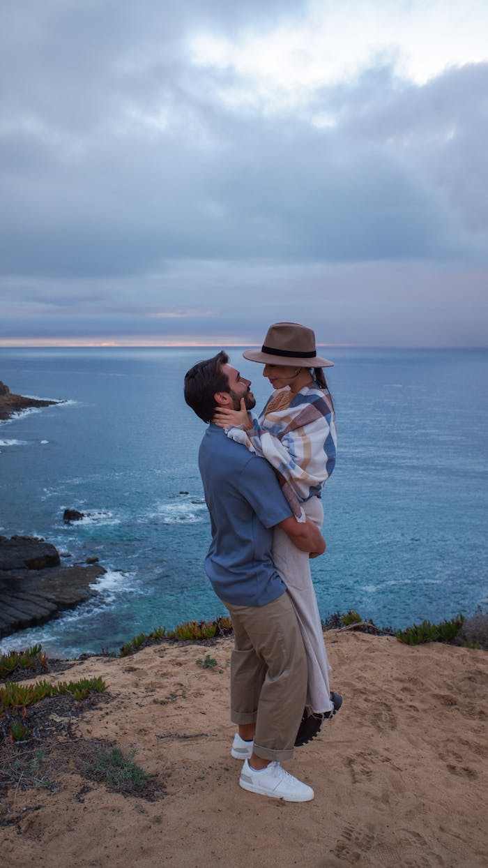 A loving couple shares a moment by the cliffside overlooking the ocean at sunset.