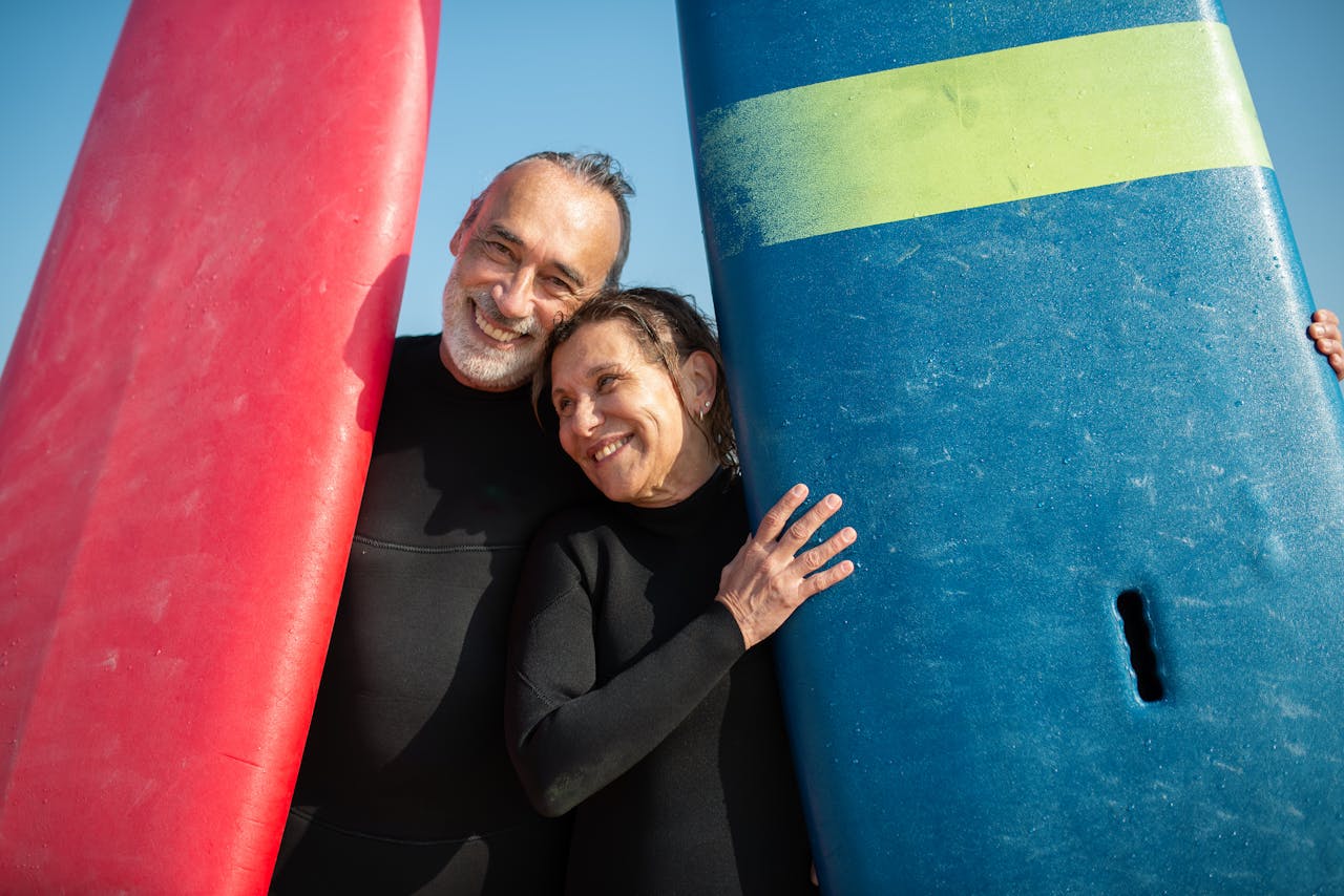 Smiling couple holding surfboards at a sunny beach, enjoying leisure time.